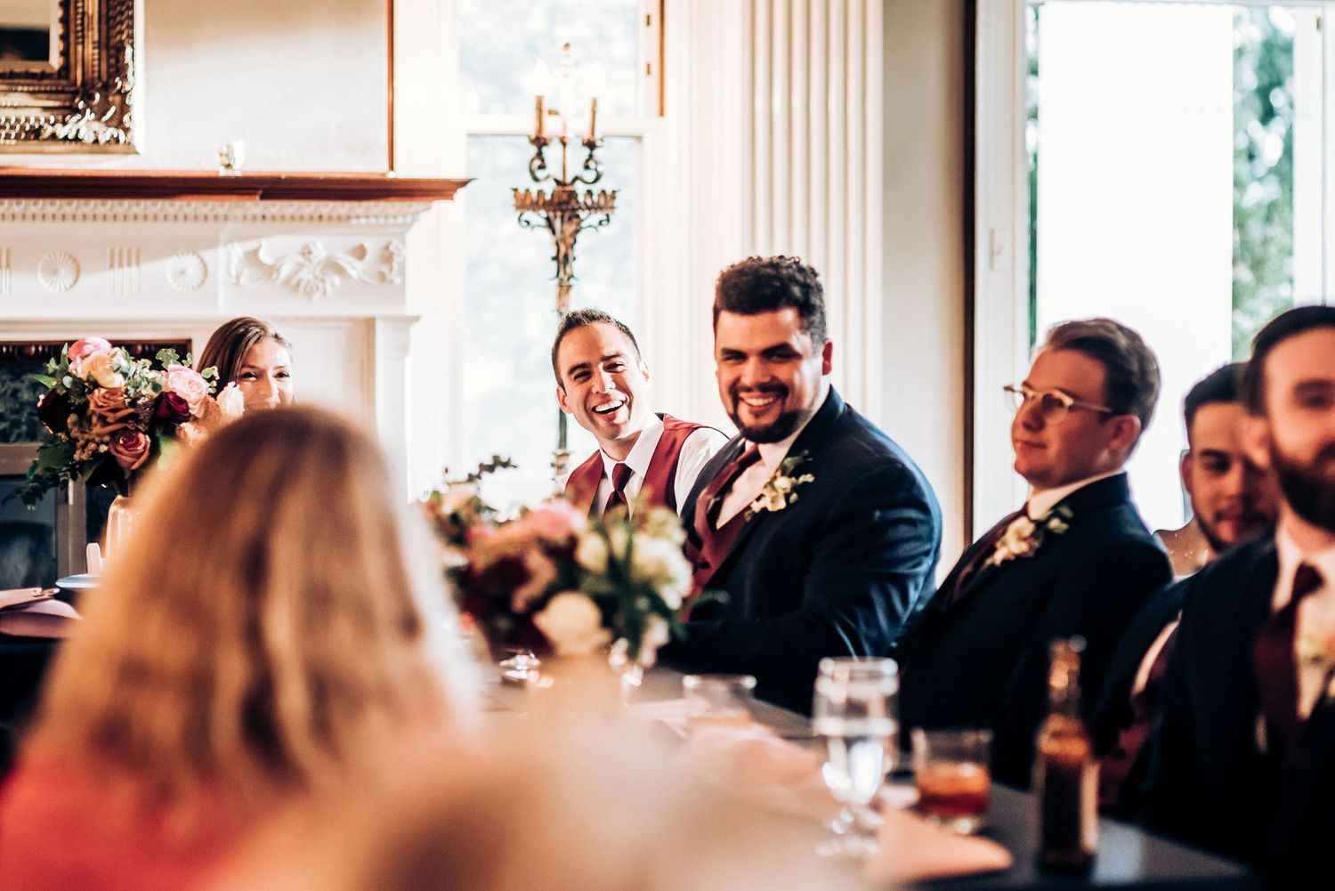 Wedding celebration in an elegant room with ornate fireplace and classic decor.