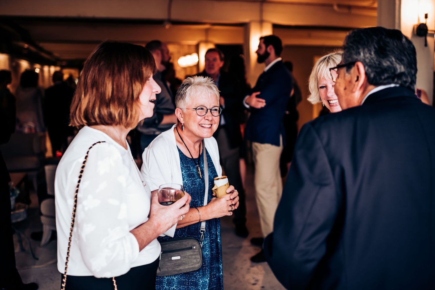 Small group enjoying drinks and conversation at an evening social gathering in a dimly lit venue.