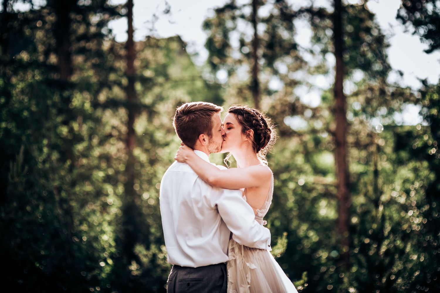 An intimate moment between newlyweds sharing a kiss in a sunlit forest.