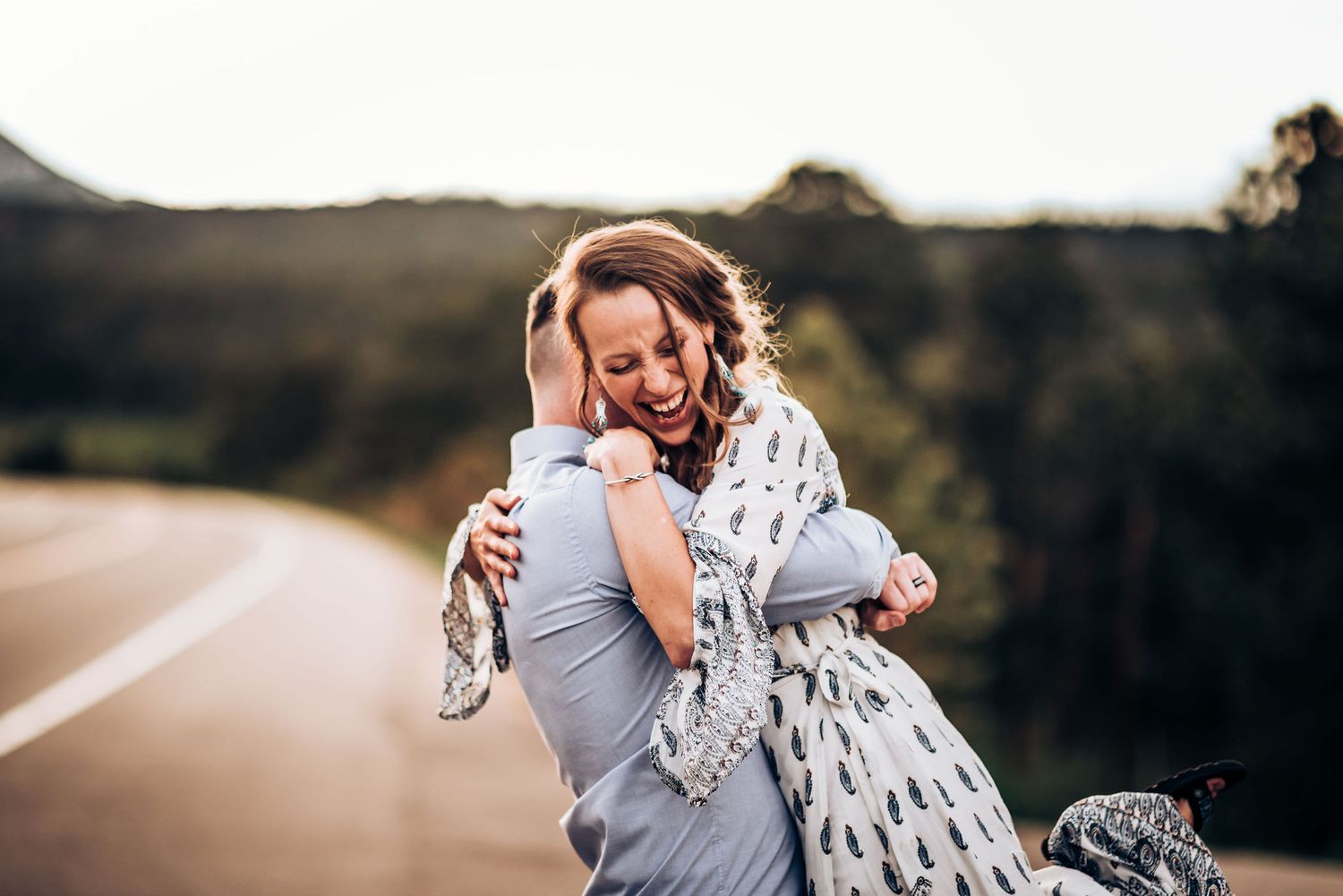 Romantic couple embracing on a mountain road during sunset in casual attire.