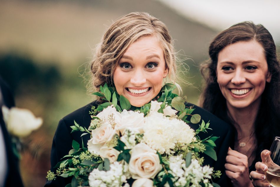 Joyful wedding moment with white rose bouquet against outdoor scenery.