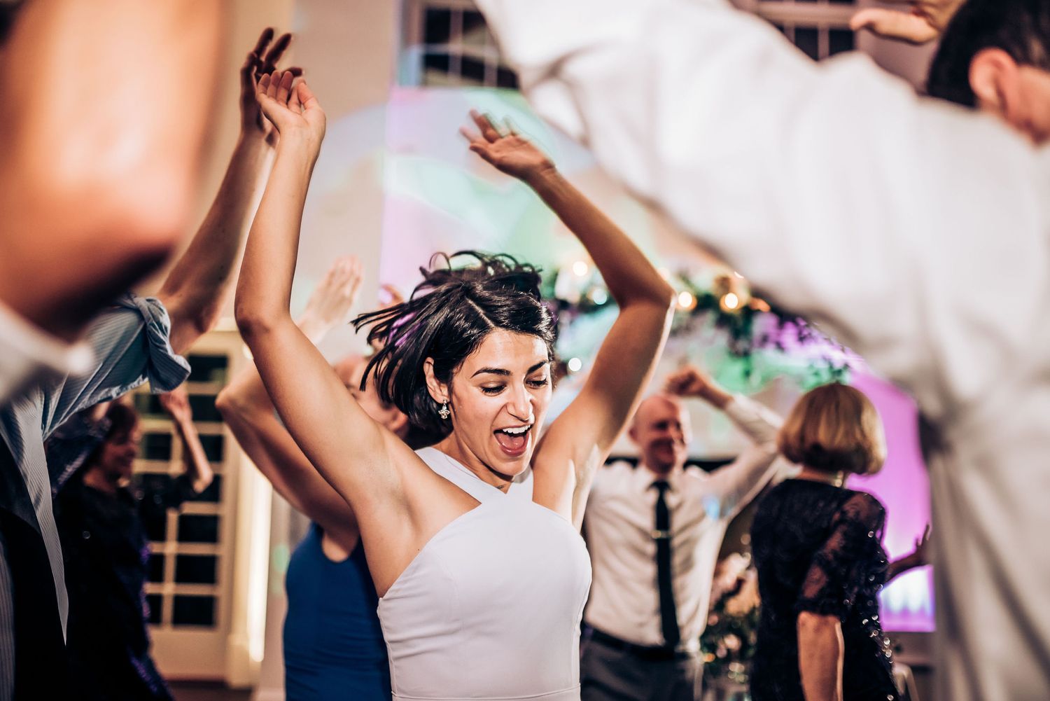 Joyful dancers celebrate at a wedding reception with raised arms and big smiles.