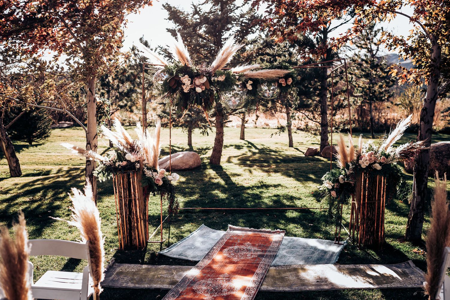 A wooden wedding arch adorned with pampas grass and floral arrangements in an outdoor garden setting.