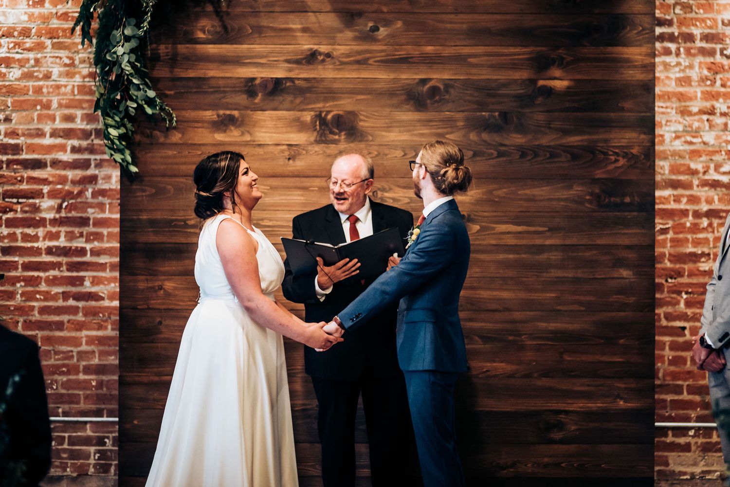 Wedding ceremony with officiant in rustic venue featuring wood paneling and brick walls.