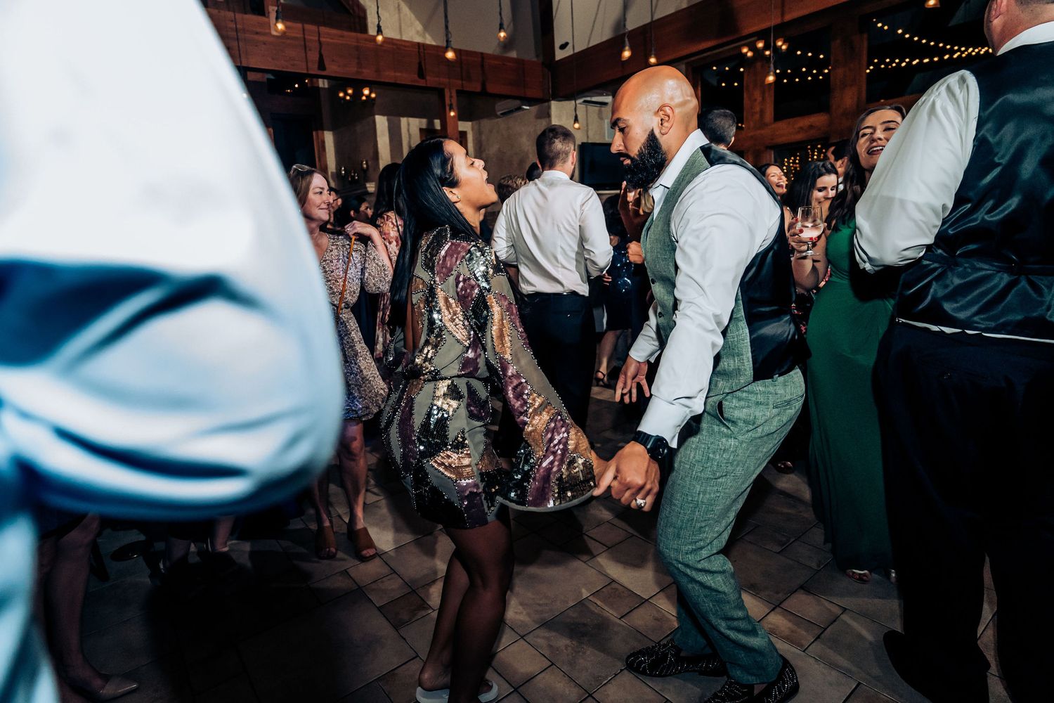 Wedding guests enjoying lively dancing on rustic wooden dance floor during reception celebration.