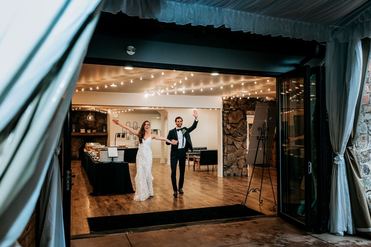 Reception dance floor through window showing couple celebrating under string lights.
