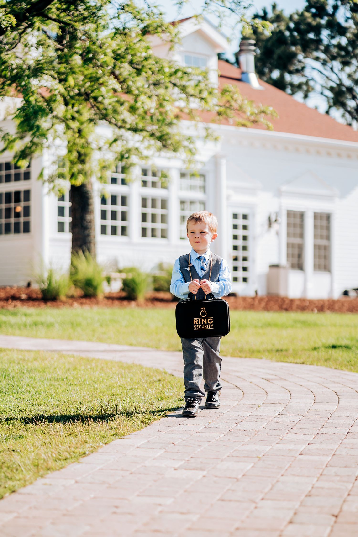 Young ring bearer in blue shirt carries black sign on stone pathway.