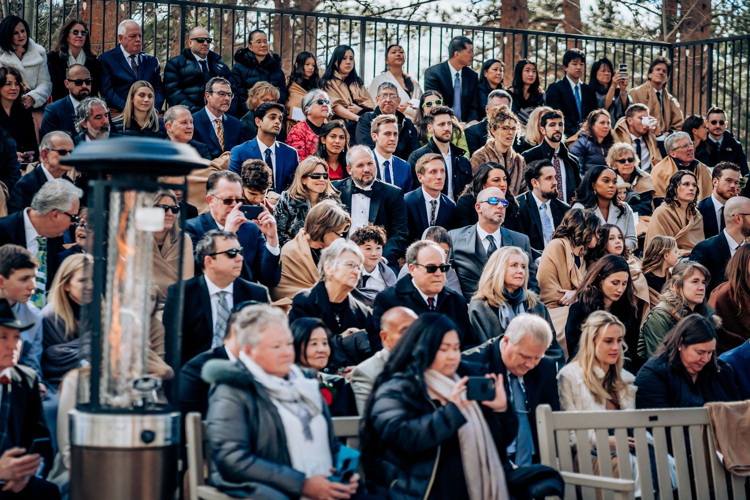 Crowd of wedding guests seated with outdoor heaters visible during winter ceremony.