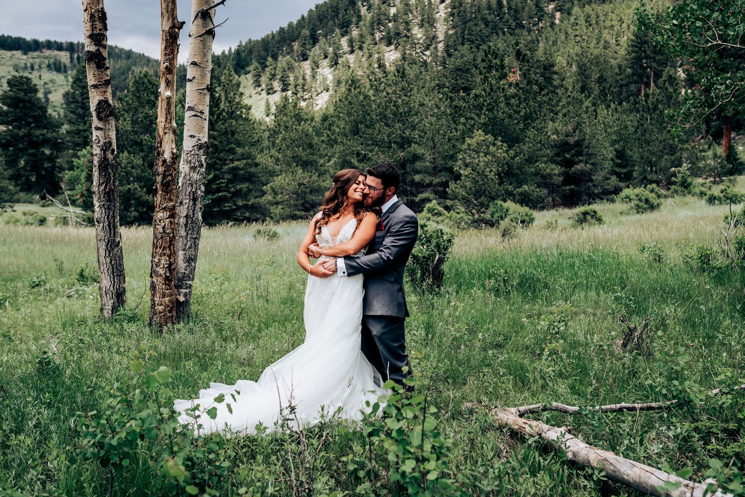 A couple embraces near birch trees in a secluded mountain meadow.