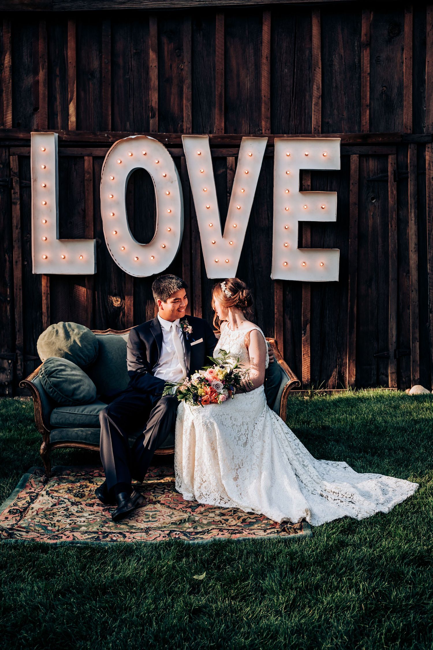 Romantic wedding portrait against wooden wall with light-up LOVE sign and vintage blue couch.