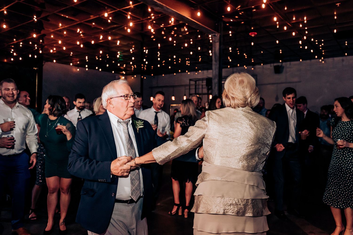 Couple dancing together at an elegant indoor reception under string lights.