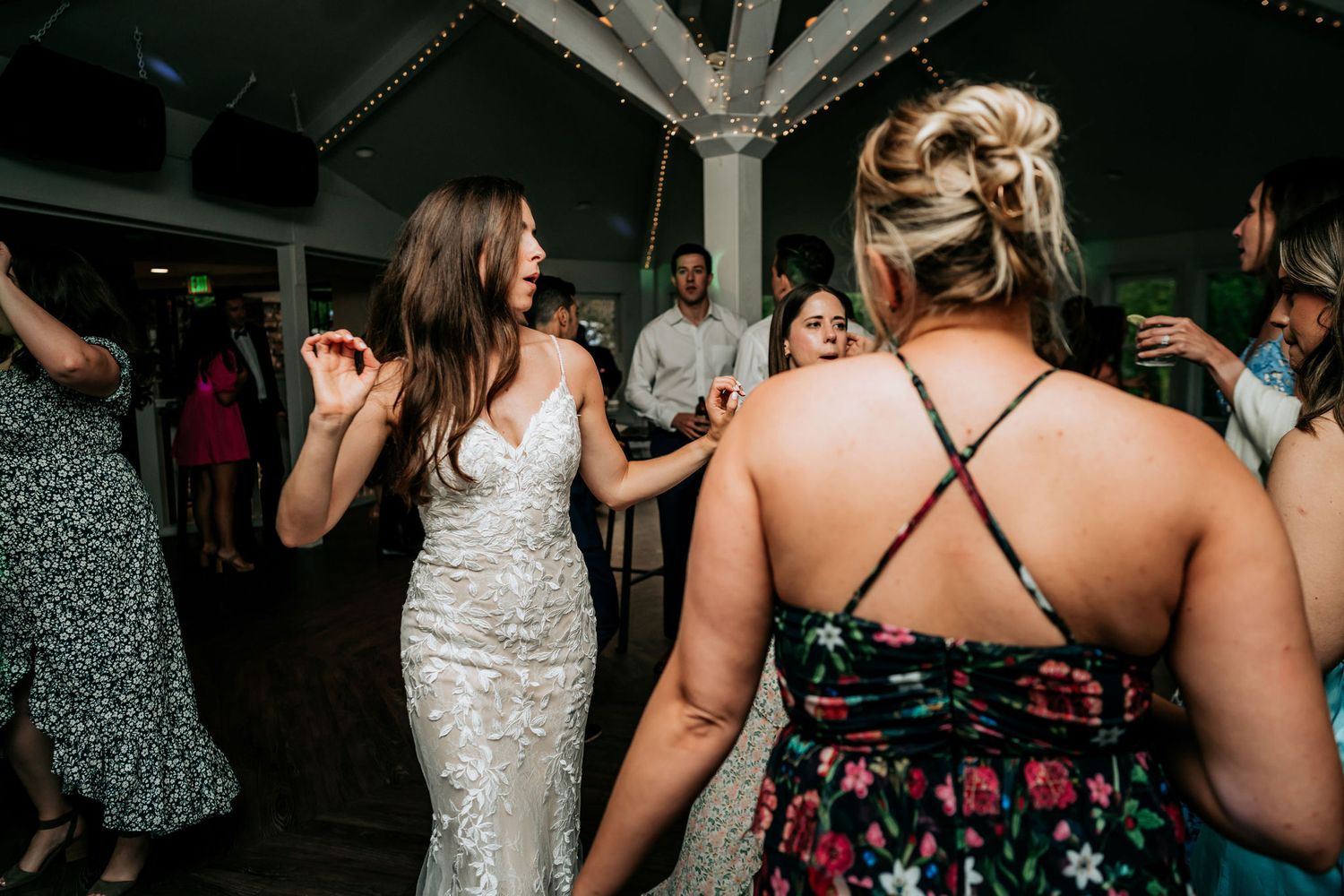 Guests dancing and celebrating at an indoor wedding reception with decorative lighting.
