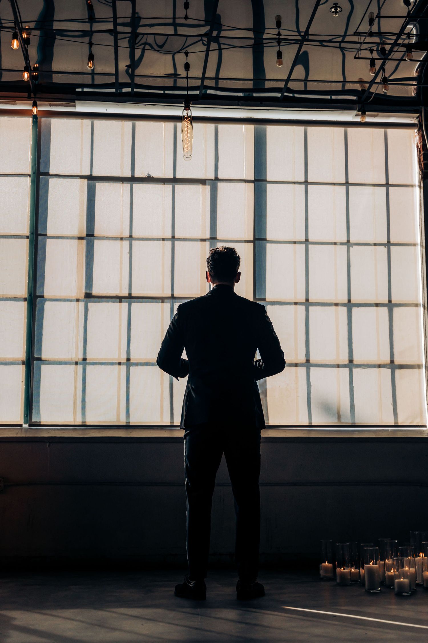 Silhouette of person standing in front of large industrial windows with dramatic backlighting.