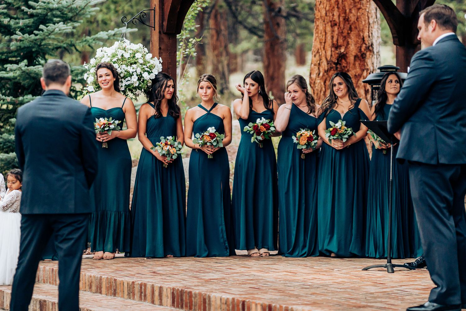 Wedding party in navy blue dresses lined up on brick steps during an outdoor ceremony.