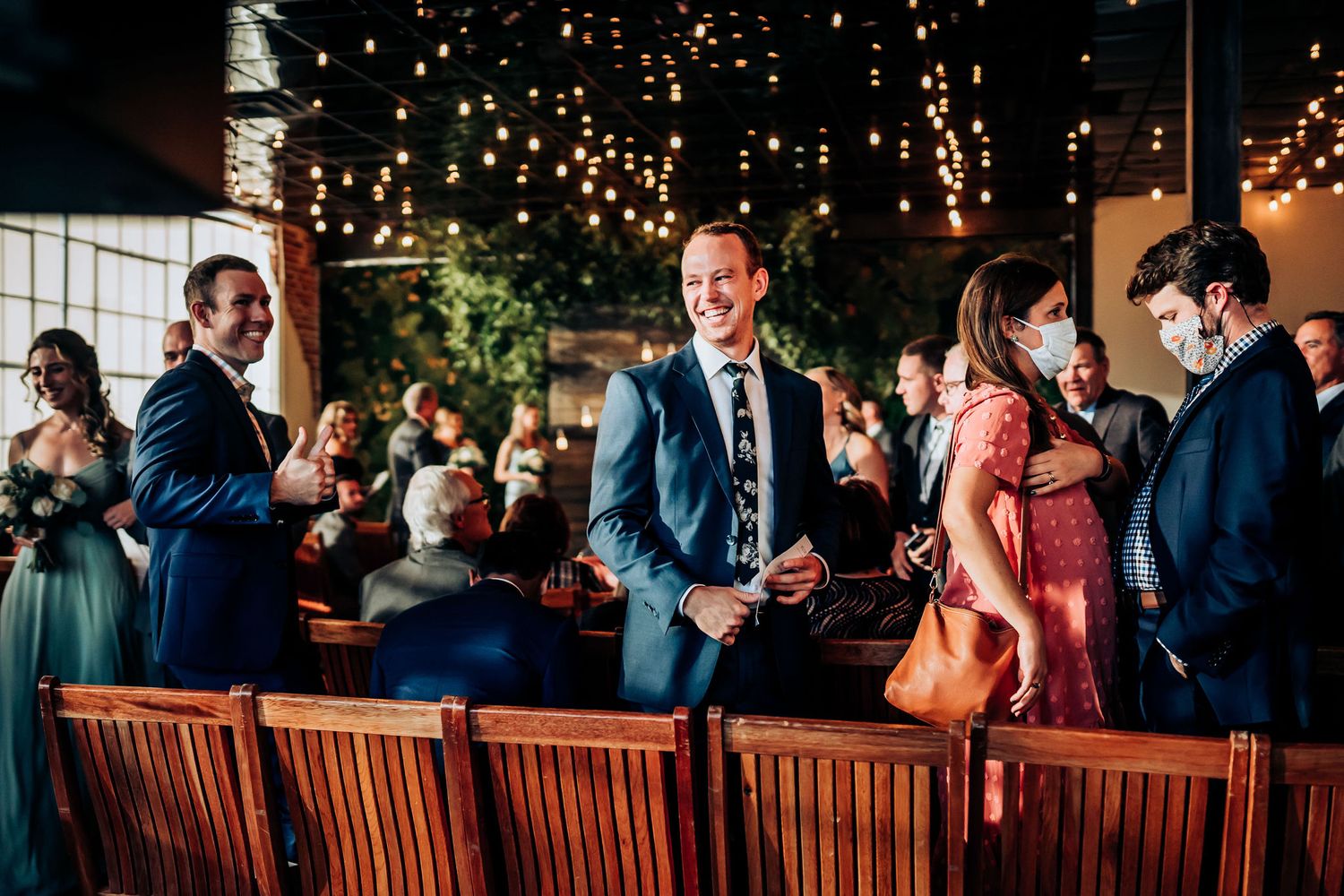 Wedding guests mingle and socialize at an indoor venue decorated with hanging string lights.