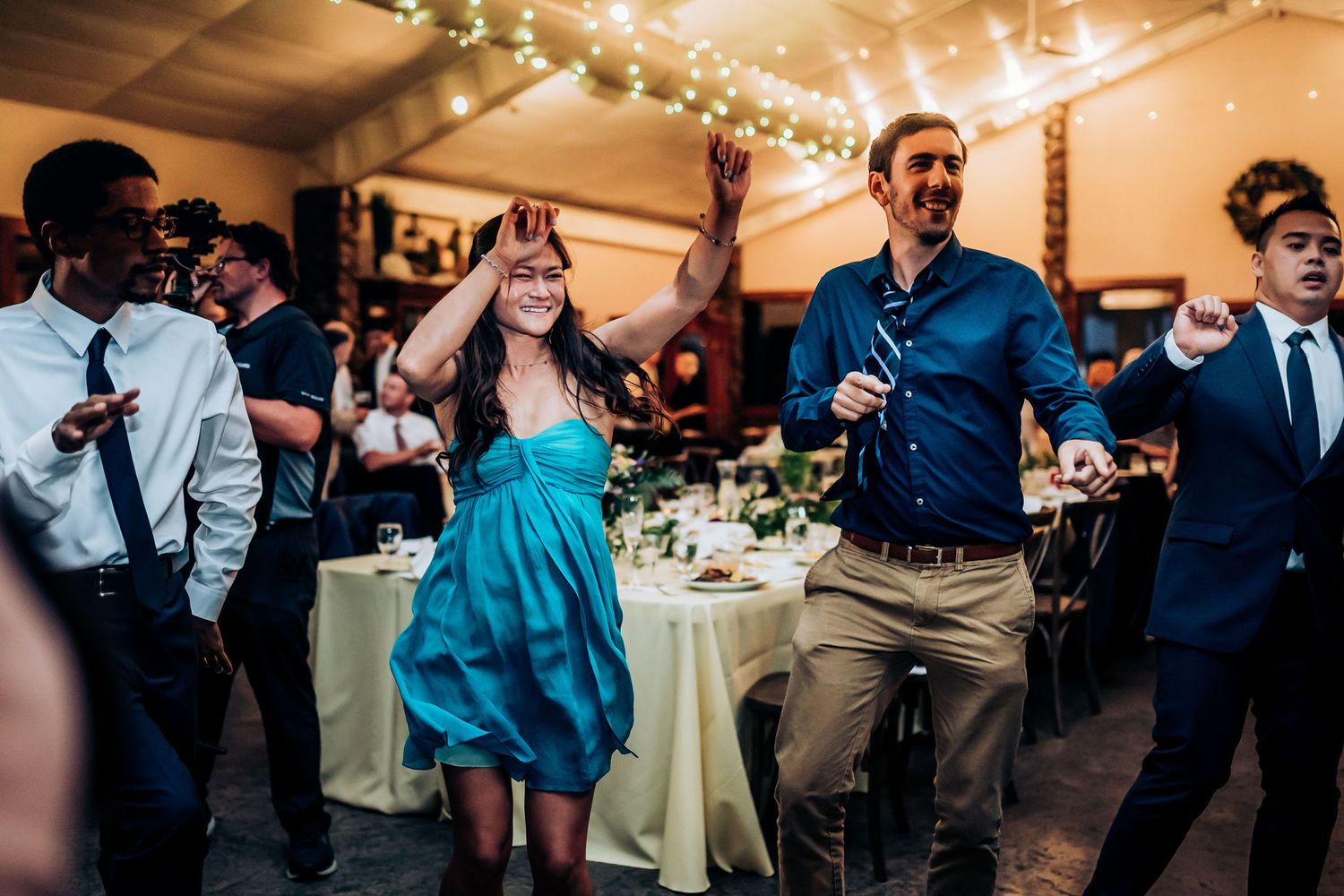 Party guests dancing and enjoying themselves at an elegant reception with twinkle lights and table settings.