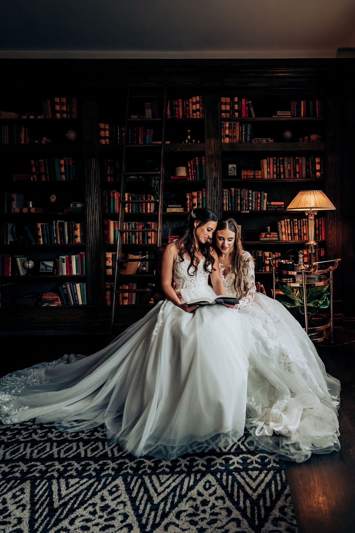 Two people in formal attire sitting on patterned carpet in library with bookshelves.