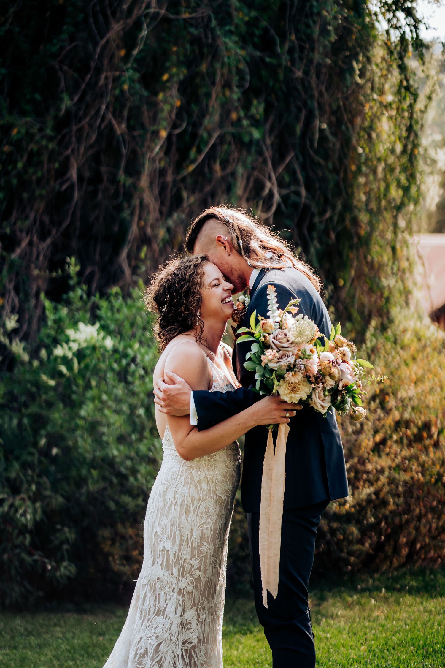 A candid wedding moment captured showing a happy couple laughing together in a garden setting.