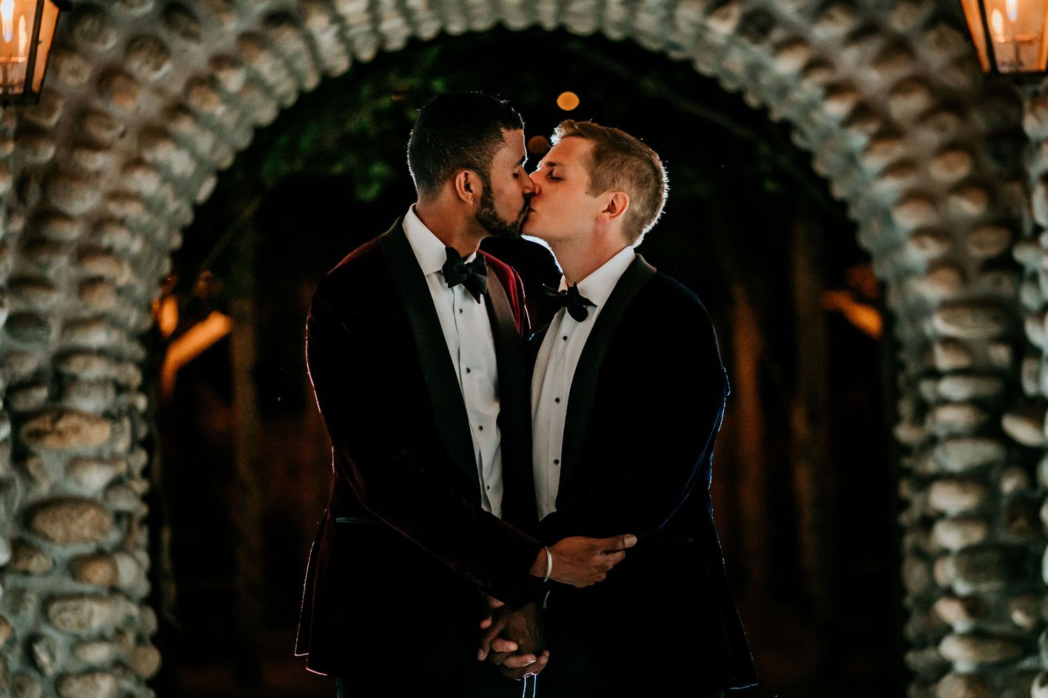 Romantic evening portrait under a stone archway lit by warm lantern light.