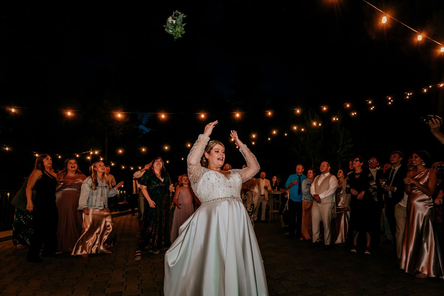 A lively dance celebration under string lights with guests dancing at an outdoor wedding reception.