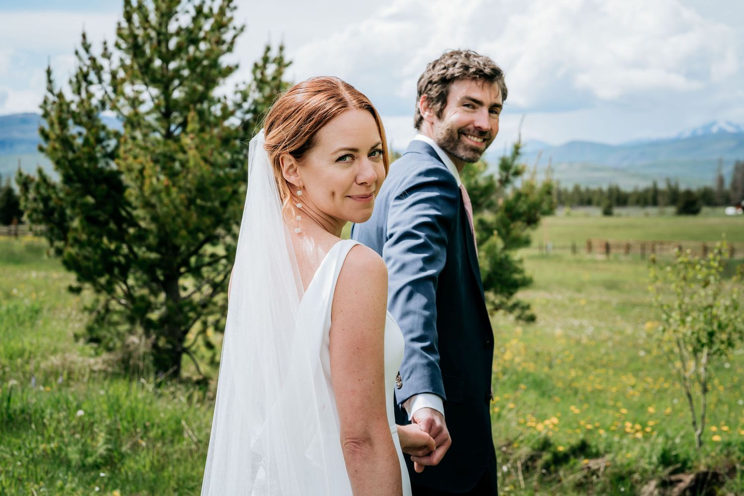 Wedding couple stands in a mountain meadow with distant hills creating a scenic backdrop.