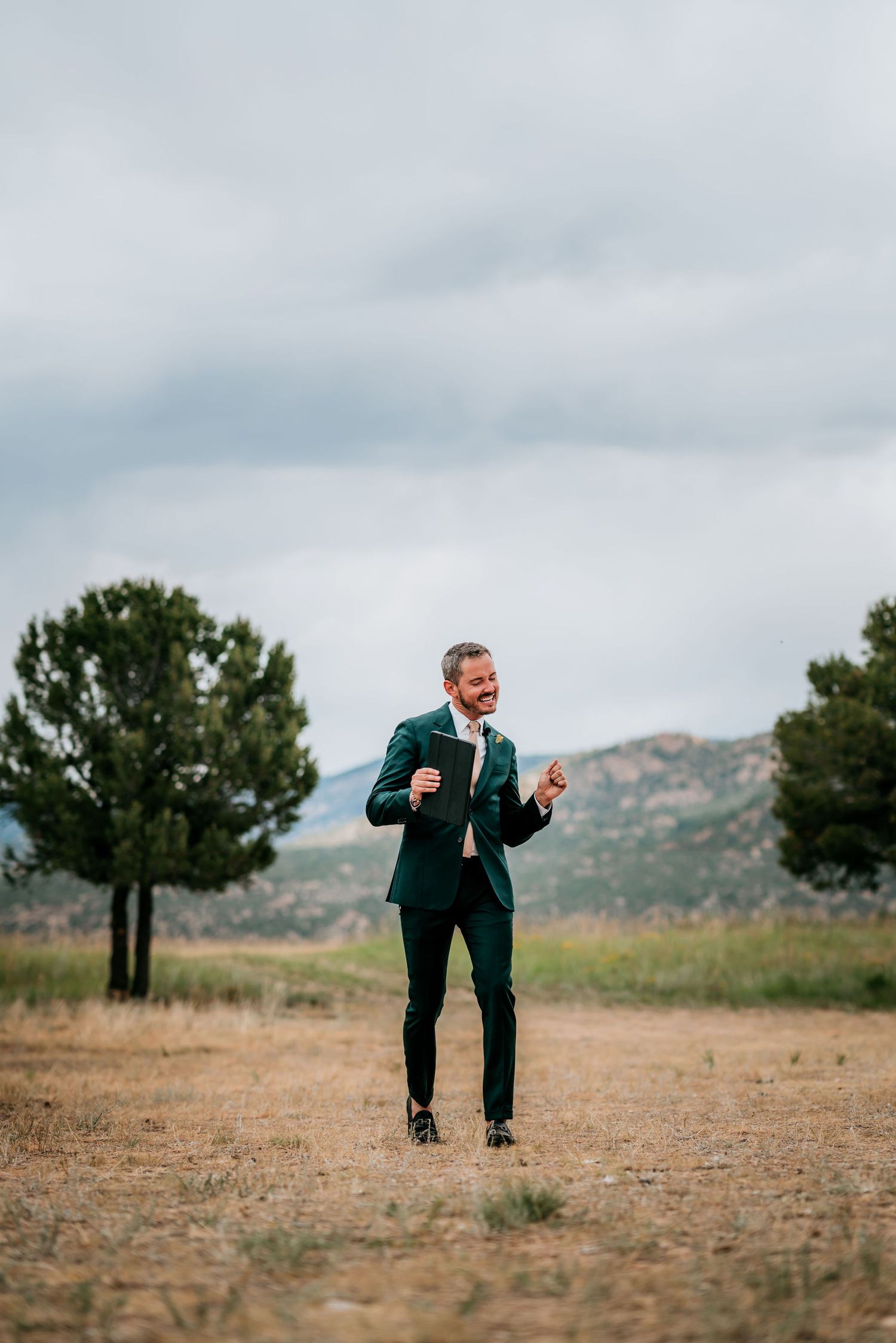 Groom celebrates with enthusiasm in a forest clearing wearing emerald green suit.
