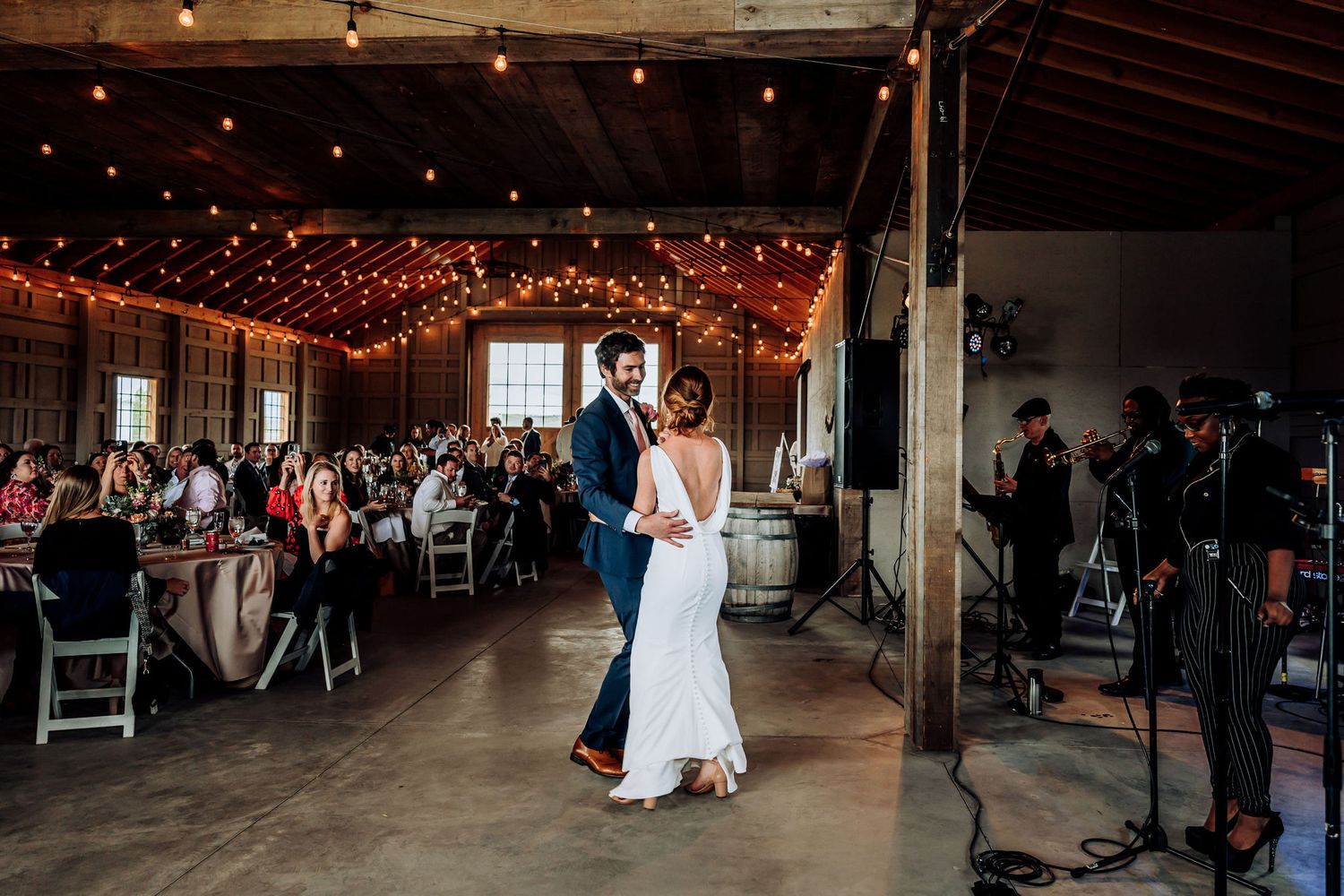 Wedding reception venue with string lights and couple dancing in rustic barn setting.