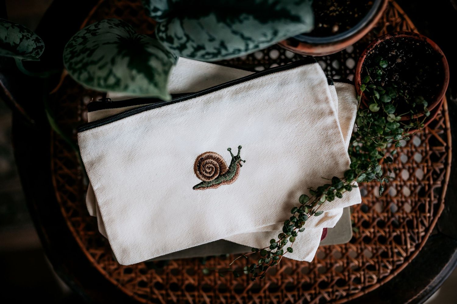 Minimalist white fabric pouch with embroidered snail design on textured background.