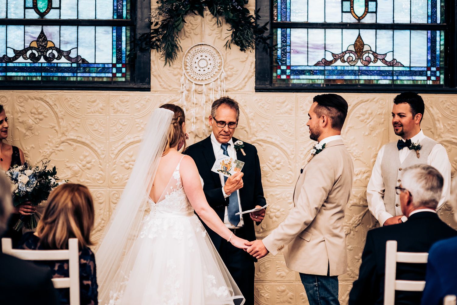 Wedding ceremony in progress beneath ornate stained glass windows and decorative archway.