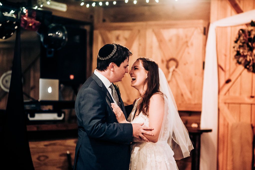 Candid wedding moment captured in rustic barn setting with string lights.