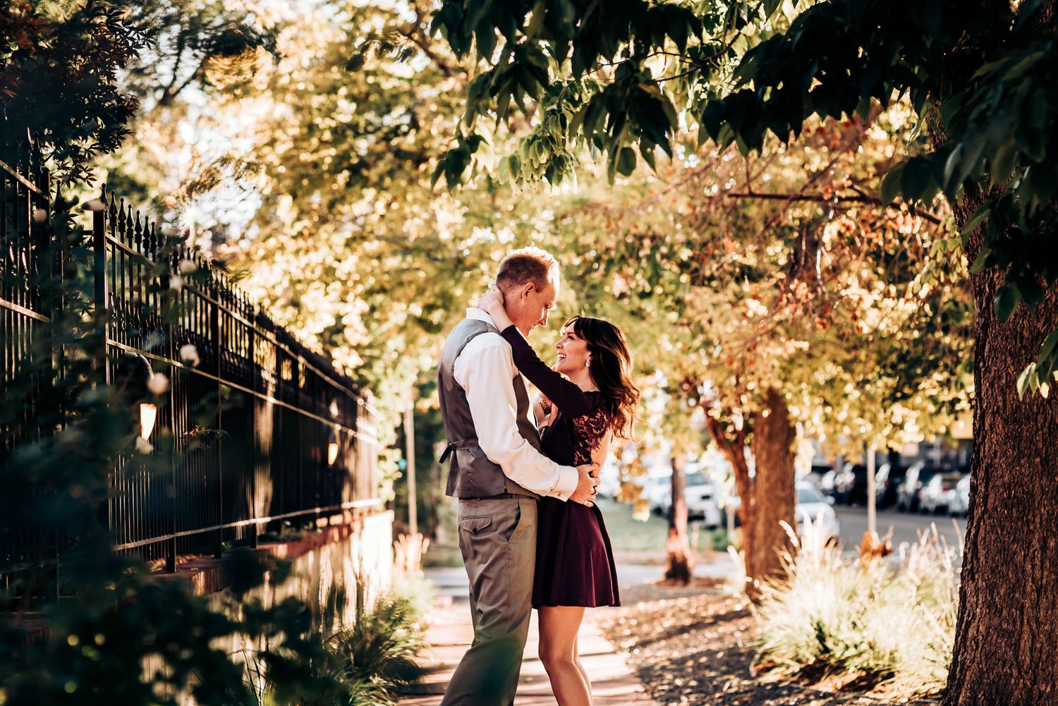 A couple shares an intimate embrace on a sunlit path surrounded by autumn trees.