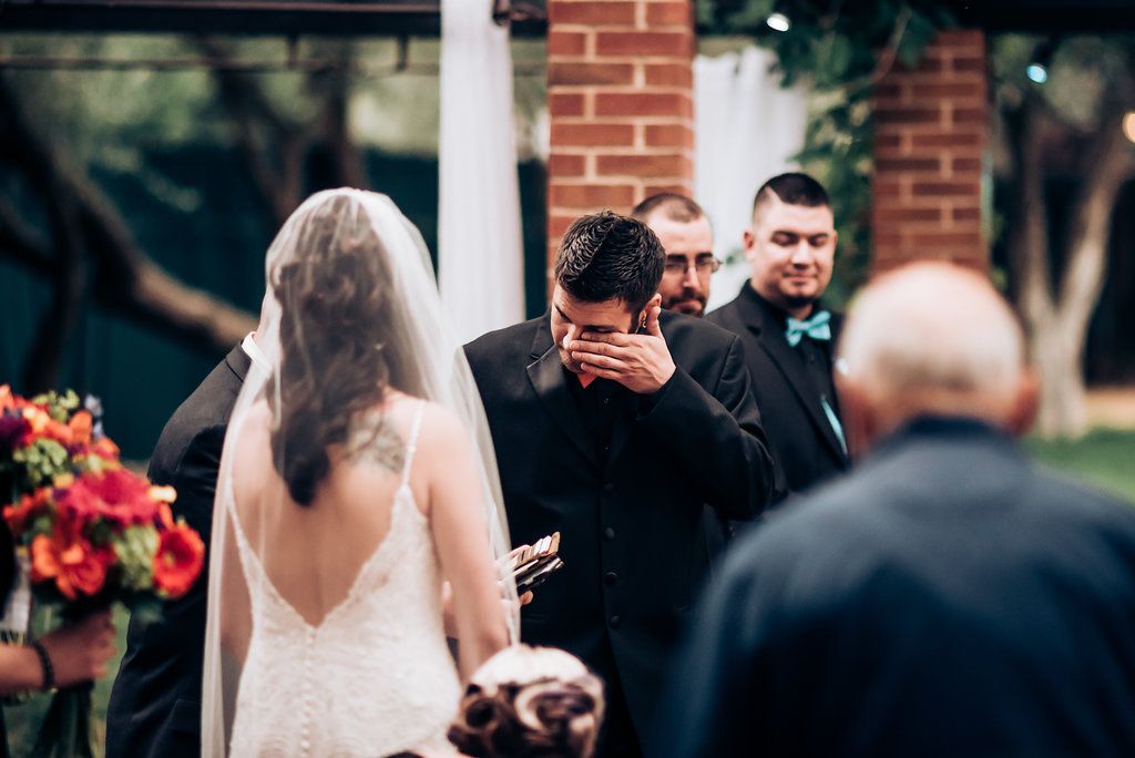 Emotional moment captured during outdoor wedding ceremony with brick pillars and floral arrangements.