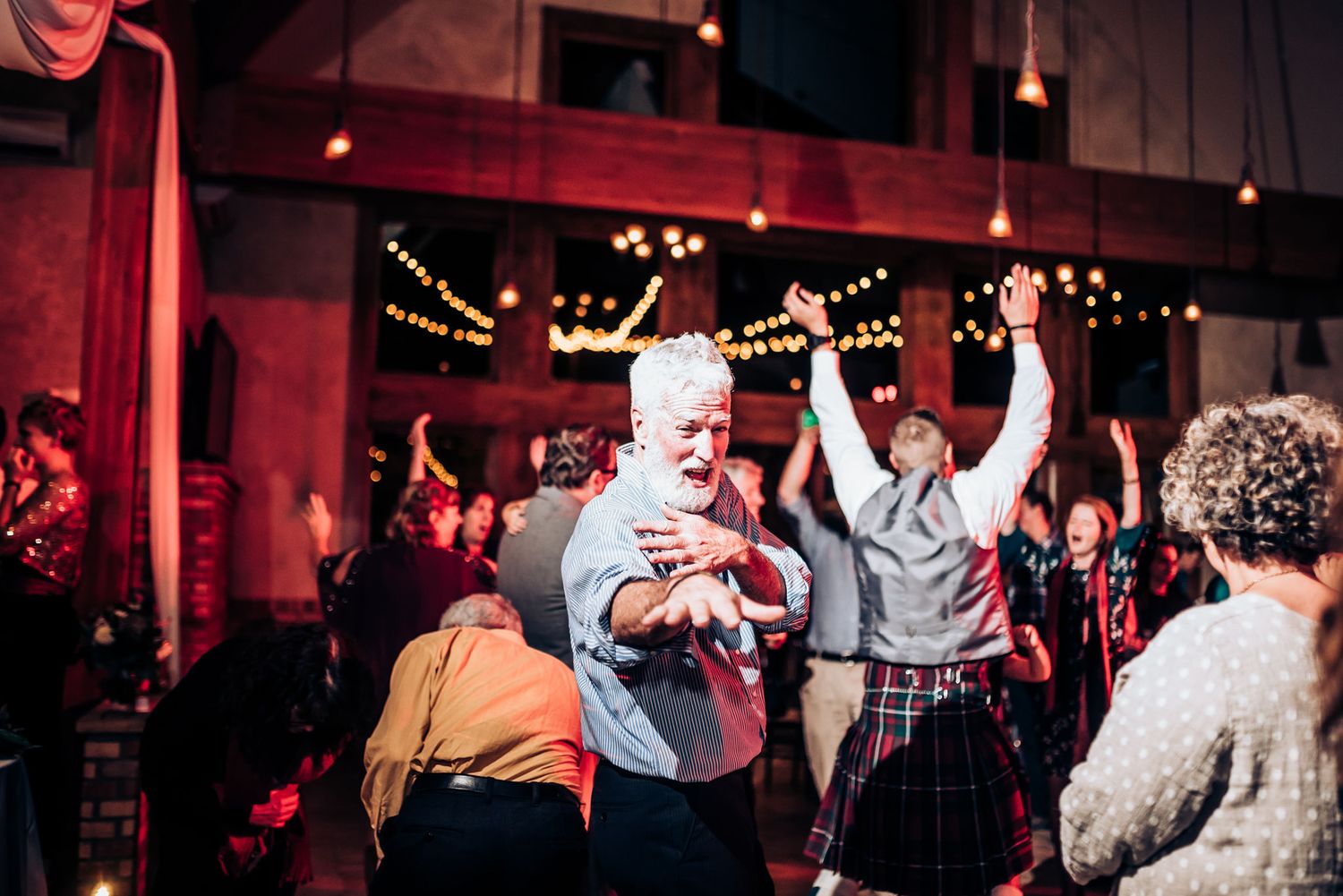Energetic dance party scene with guests celebrating on the dance floor under string lights.