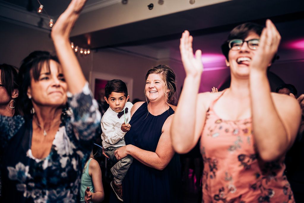 Joyful guests dancing and celebrating at a wedding reception with festive lighting.