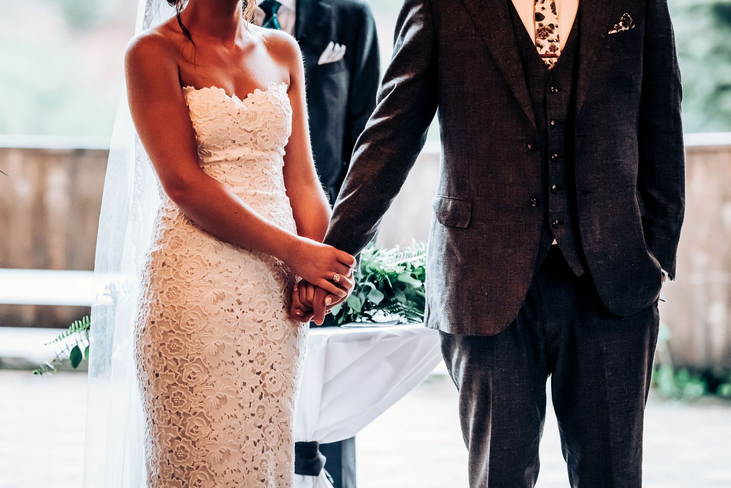 A couple stands together at their wedding ceremony with the bride wearing an elegant lace gown.