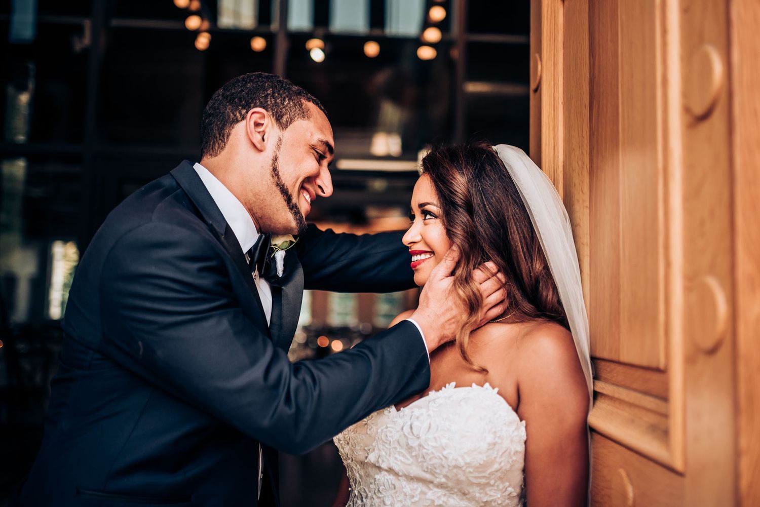 Joyful wedding couple shares laughter and emotion in front of wooden church doors.