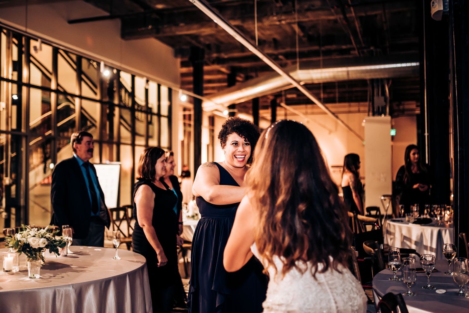 Party guests socializing and dancing at an industrial-style venue with warm lighting.