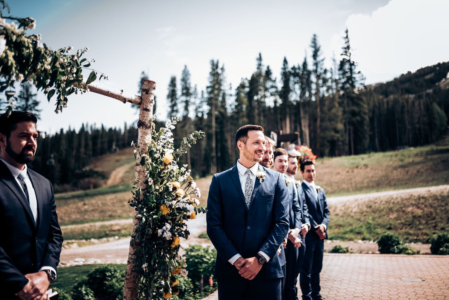 Groomsmen in navy suits watching emotional ceremony reaction at mountain venue.