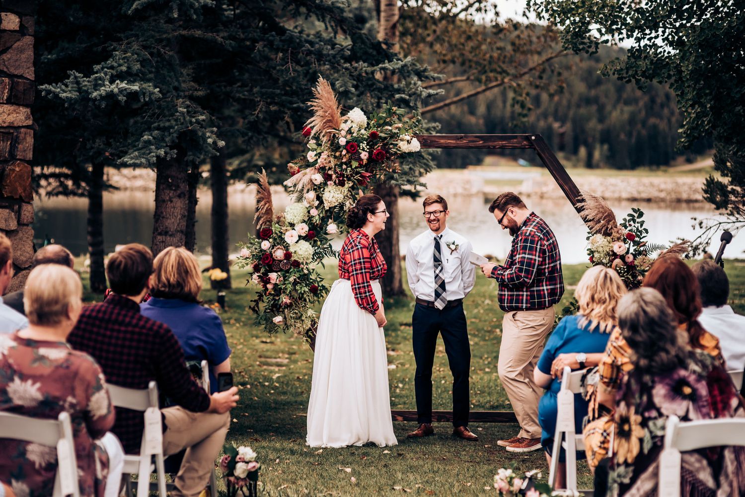 Wedding guests watch the ceremony from white chairs on a lawn with mountain and lake views.