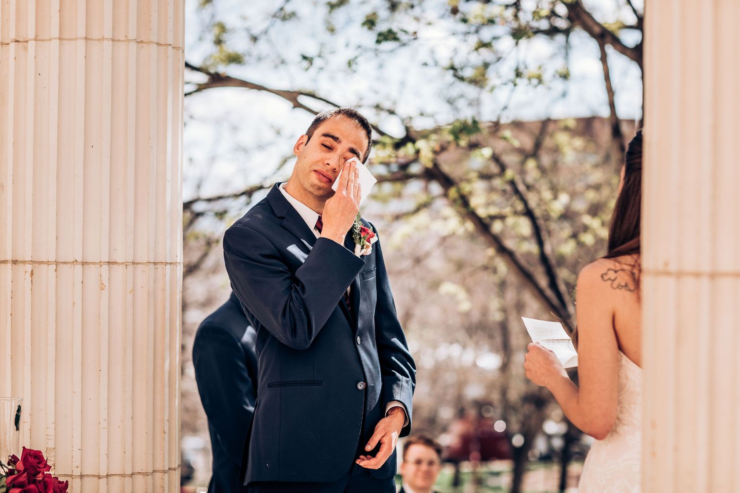 Emotional moment at outdoor wedding ceremony captured between classical columns.