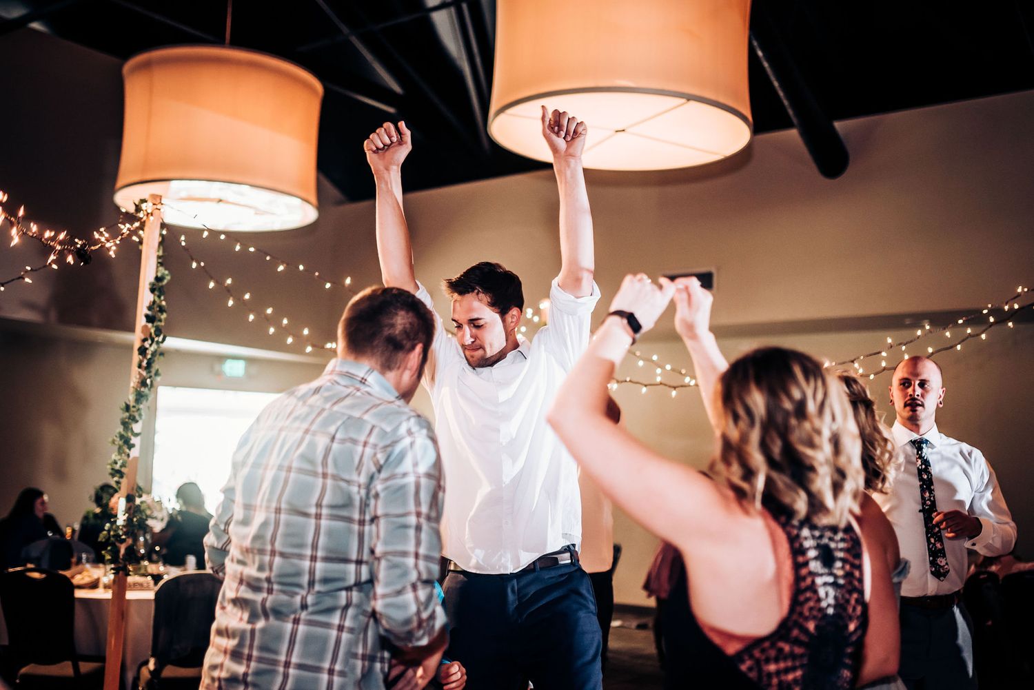 Energetic dancing and celebration under warm pendant lights at indoor wedding reception.