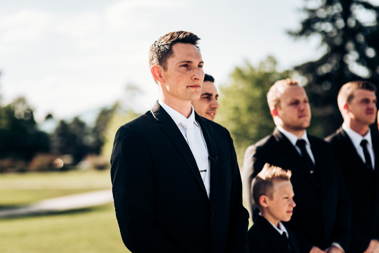 Wedding party members in formal attire standing outdoors on a sunny day.