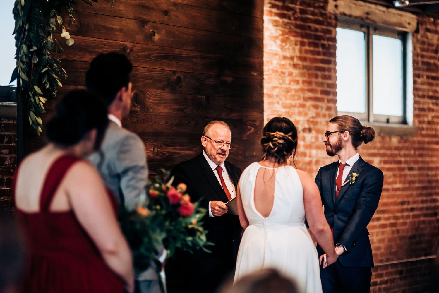 Intimate wedding ceremony taking place in industrial-style venue with exposed brick walls.