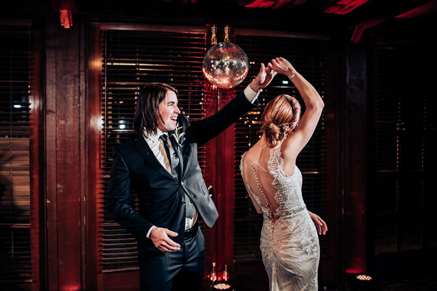 A couple dances energetically under a disco ball at their wedding reception.