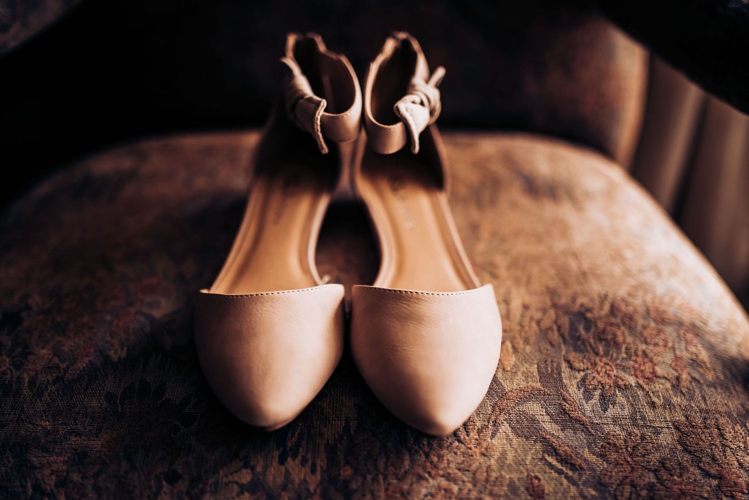 Nude colored bridal flats arranged on a textured brown leather surface.