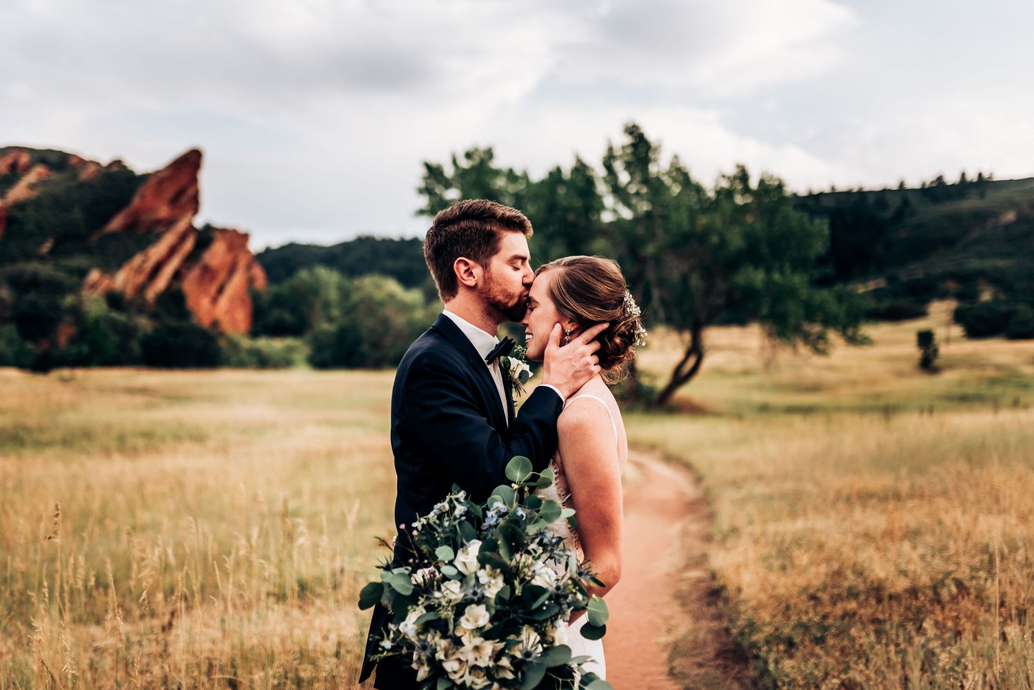 Couple shares intimate moment in formal attire with mountain landscape behind them.