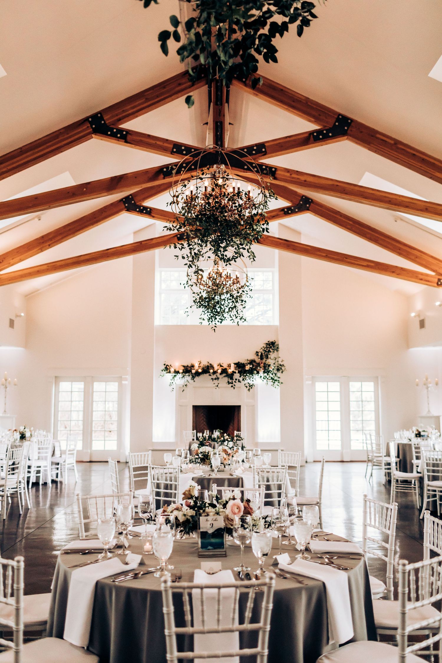Elegant wedding reception venue with vaulted wooden beam ceiling and hanging greenery chandeliers.