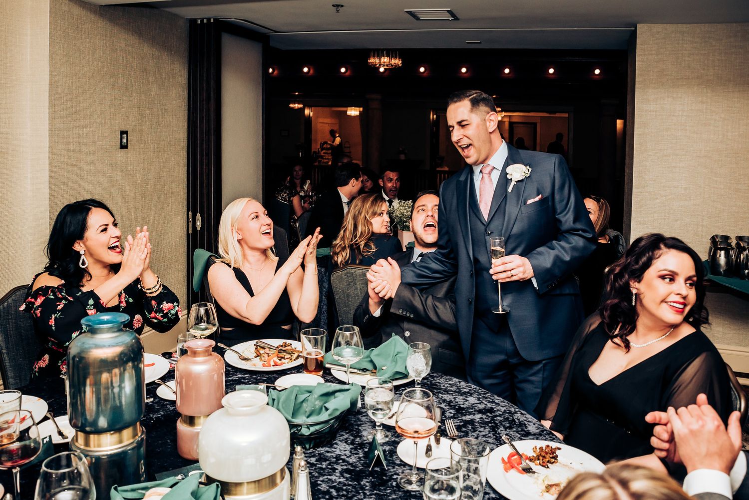 Wedding guests share laughter around a decorated dinner table during an indoor reception.