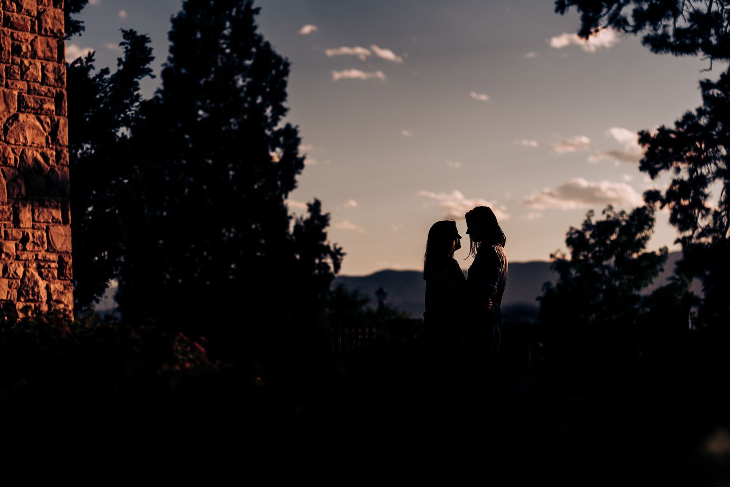Silhouetted figures in romantic pose against dusky sky and stone building.