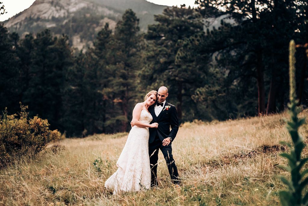 A wedding couple embracing on a mountainside with dramatic rocky peaks in the background.